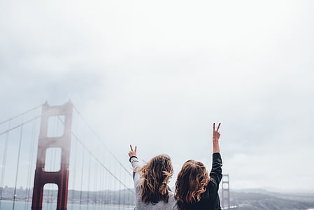 two women raising hands near Golden Gate bridge at daytime thumbnail