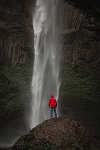 man standing on cliff in front of waterfalls during daytime thumbnail