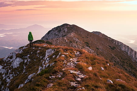 person wearing green bubble jacket standing over rocky cliff under cloudy sky thumbnail