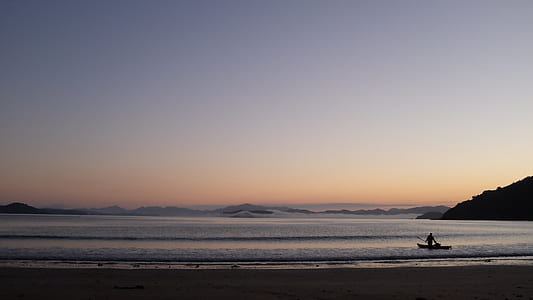 silhouette of person on boat by shore during golden hour thumbnail