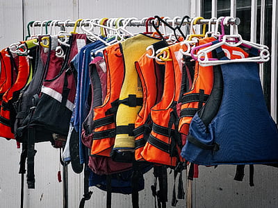 assorted-color life vest lot on grey rack near white wall thumbnail
