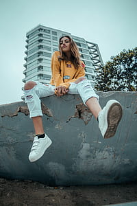 woman in white distressed jeans sitting on gray wall thumbnail