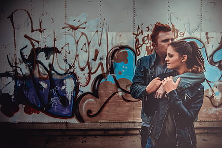 man and woman in blue denim jacket standing near graffitti thumbnail