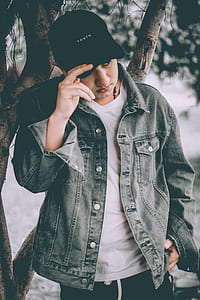 man in denim jacket standing near tree during daytime thumbnail