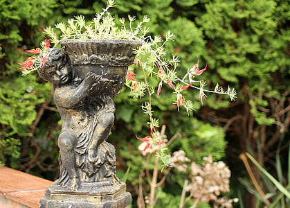 cherub holding pot near green leafed plant thumbnail