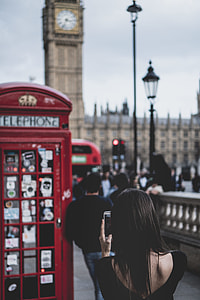 black haired woman standing near red phone capturing big ben tower clock thumbnail
