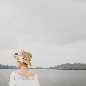 woman with woven hat facing body of water thumbnail