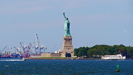 Statue of Liberty with boat traffic and cranes as viewed from a Staten Island Ferry crossing New York Harbor on its way to Staten Island. thumbnail