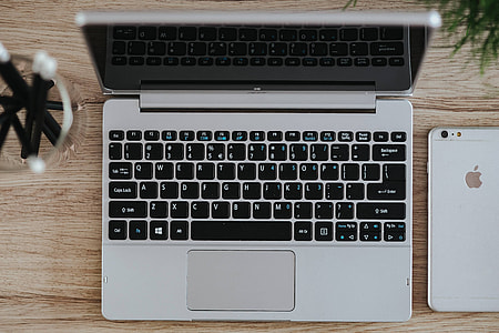Silver Acer laptop on a wooden desk with a green plant, pencils and an Apple iPhone thumbnail