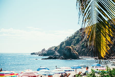 A tropical beach full of tourists with a cliff in the background thumbnail