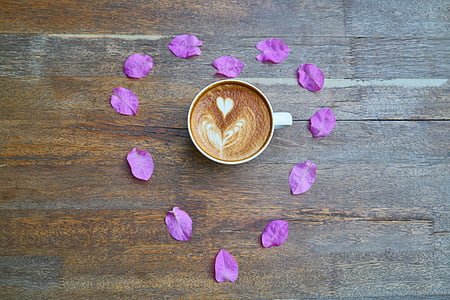white ceramic teacup filled with coffee surrounded with pink flower petals thumbnail