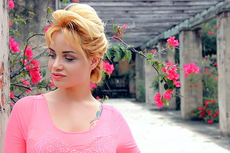 woman in pink shirt standing near flowers thumbnail