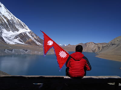 Man sitting on the shore of Tilicho Lake in Nepal, holding flag. thumbnail