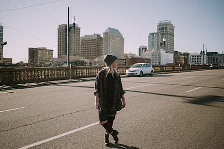woman standing at the road near car and buildings at the distance during day thumbnail