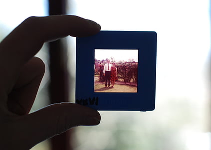 person holding digital photo frame displaying man and woman taking groupie beside fence thumbnail