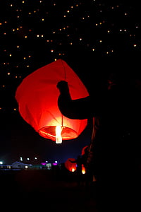 man holding lighted sky lantern at night time thumbnail