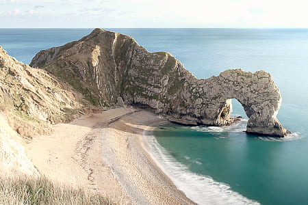 person taking photo of rock formation near body of water thumbnail