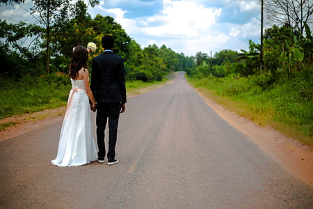 bride and groom standing on asphalt road beside trees during daytime thumbnail