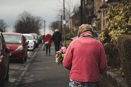 woman walking on sidewalk holding bouquet of pink flowers thumbnail