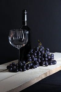 grapes beside wine bottle and empty wine glass on brown wooden plank thumbnail