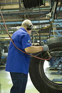 man wearing blue polo shirt holding tool and vehicle tire thumbnail