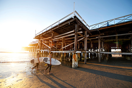 two people holding surfboards walking near pier thumbnail