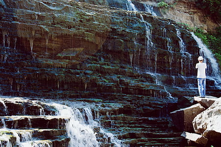 Man in White T-shirt and Blue Jeans Standing Near Water Falls thumbnail