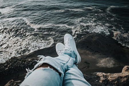 person in jeans sitting on rock looking at the sea thumbnail