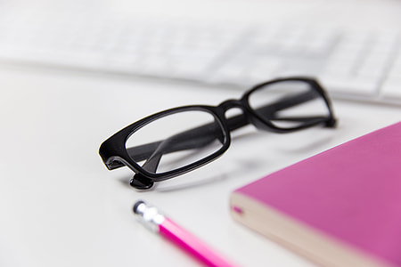 Reading glasses on a white office desk with computer keyboard, notepad and pencil thumbnail