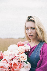 woman holding rose flowers standing on open field during daytime thumbnail