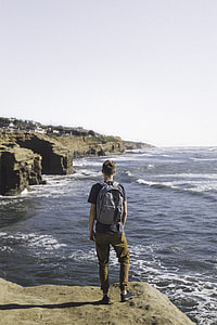 man standing on rock looking on body of water during daytime thumbnail