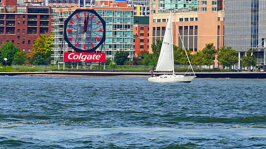 A small sailboat sails up the Hudson River pass the Colgate clock in Jersey City. thumbnail