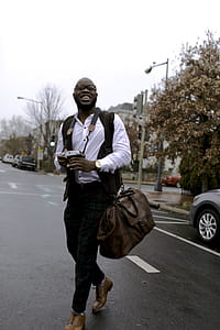 Man in White Button-up Dress Shirt Holding Camera While Smiling and Crossing Street thumbnail