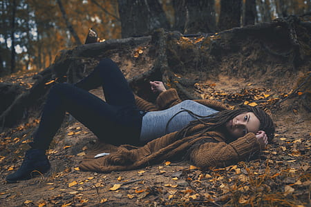 woman wearing brown cardigan and gray t-shirt with black sweatpants laying in forest during daytime thumbnail