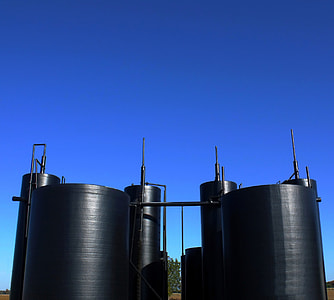 low-angle photography of two black industrial fuel tanks under calm blue sky thumbnail