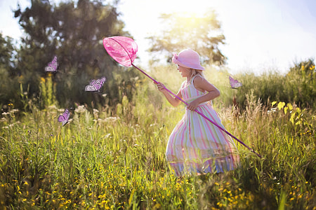 girl capturing butterfly on high vegetation ground during daytime thumbnail