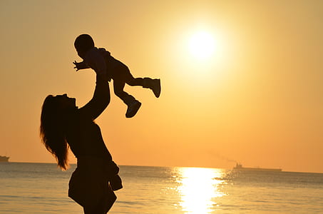 silhouette lifting her baby upward near sea during sun set thumbnail