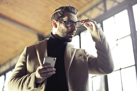 Young Adult Man removing his glasses with the right hand and holding a cellphone his left hand thumbnail