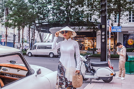 Woman Wearing White Dress Standing at Side of a Vehicle Parked at a Curb thumbnail