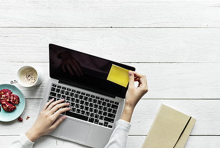 person typing on laptop while placing yellow sticky note on laptop monitor thumbnail