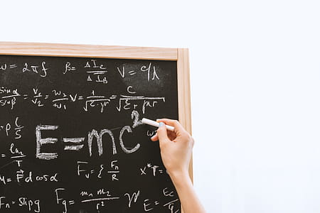Female hand holding white chalk in front of a blackboard with Einstein formula. Education and school concept. thumbnail