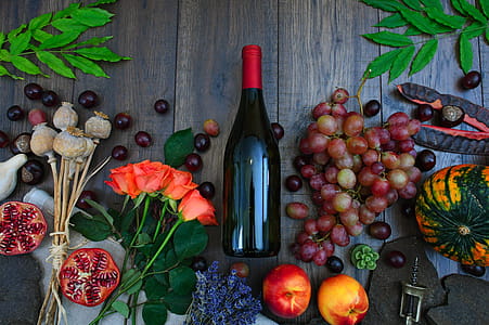 Wine Bottle Beside Grapes, Roses and Several Fruits on Brown Wooden Surface thumbnail