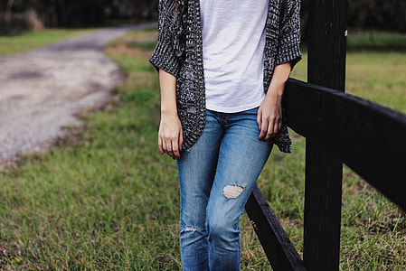 woman in white shirt and black cardigan leaning on brown wooden fence thumbnail