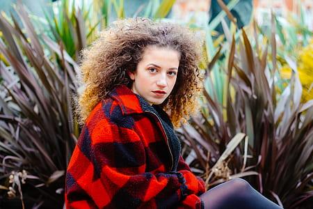 woman wearing red and black jacket sitting near plants thumbnail