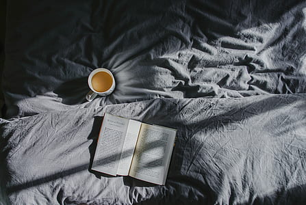 open book near mug on bed cover thumbnail