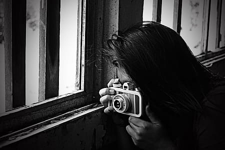 Grayscale Photo of Woman Taking Photo Beside Window thumbnail