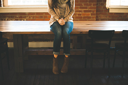 woman sitting on brown wooden table near window inside room thumbnail