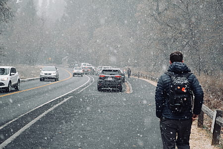 person walking on road beside moving vehicles during winter thumbnail