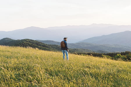 man standing on green grass field facing mountain during daytime thumbnail