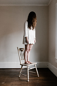 woman in white long-sleeved dress standing on white wooden chair near corner of the room thumbnail